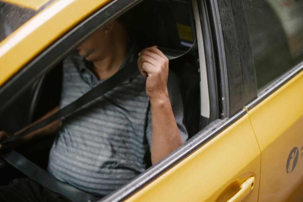 pexels-photo-5834963 A man securely fastens his seatbelt inside a yellow taxi, emphasizing safety during urban transport.